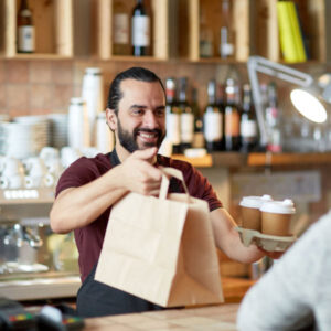 A dedicated local retail shopkeeper hands over a paper bag filled with goods to a satisfied customer. This interaction highlights the essence of community commerce, emphasizing the importance of supporting small businesses and the unique personal touch they bring to the commercial real estate landscape in their community.