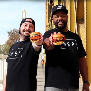 Two proud restaurant owners in Sacramento, holding up a meticulously crafted sandwich, a symbol of their culinary expertise. The image emphasizes the importance of securing the right commercial real estate location, a journey guided by Capital Rivers to ensure restaurateurs find the perfect backdrop for their gastronomic ventures.