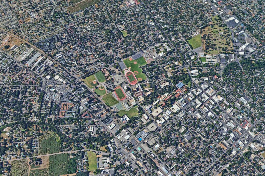 Aerial view of Chico Real Estate, California, showcasing Bidwell Park's green expanses and the historic downtown area nestled in the Sacramento Valley landscape