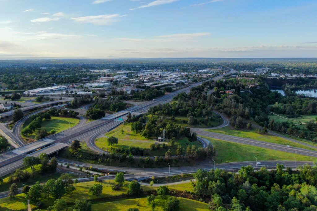 An aerial view of Redding, CA, showcasing the city's transformation with new projects by Capital Rivers Commercial aimed at enhancing community life and boosting the local economy. The image highlights welcoming parks, refreshed shops, and state-of-the-art healthcare facilities as part of Redding's exciting developments.