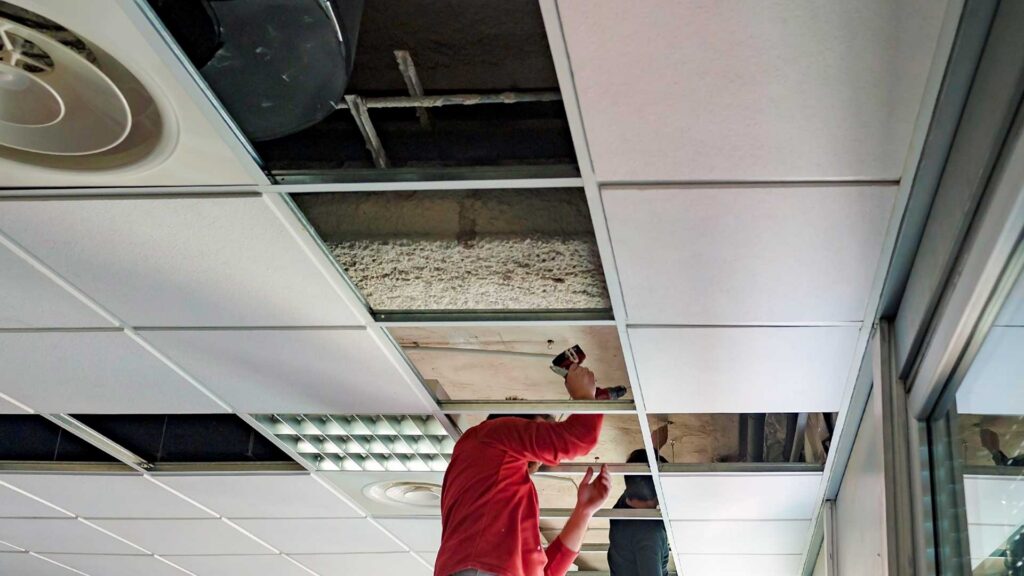 Worker repairing a drop ceiling, showing property obsolescence in real estate